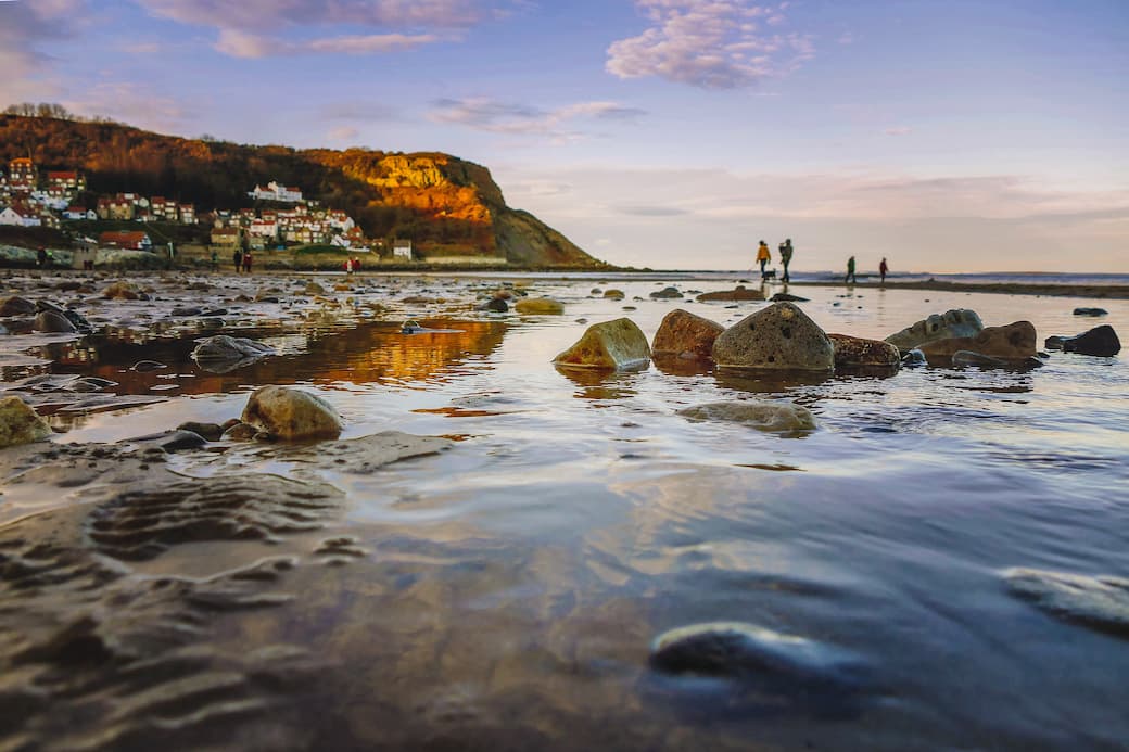 Close-up image of the water at Runswick Bay in Yorkshire, with people and houses in the distance_The best UK holiday destinations for families