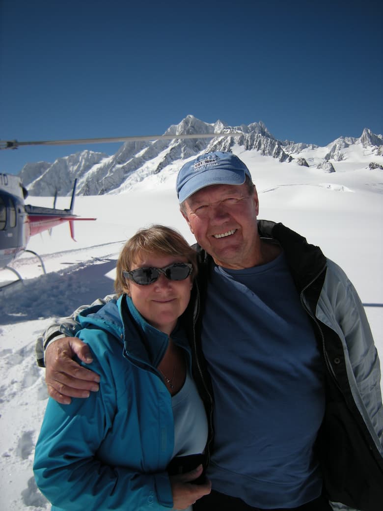 Lady and man on a snowy mountain with a helicopter in the background_HomeExchange